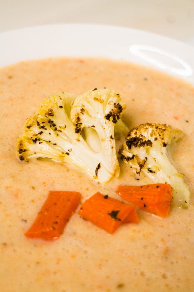 rcloseup of roasted cauliflower and carrots on top of creamy soup.