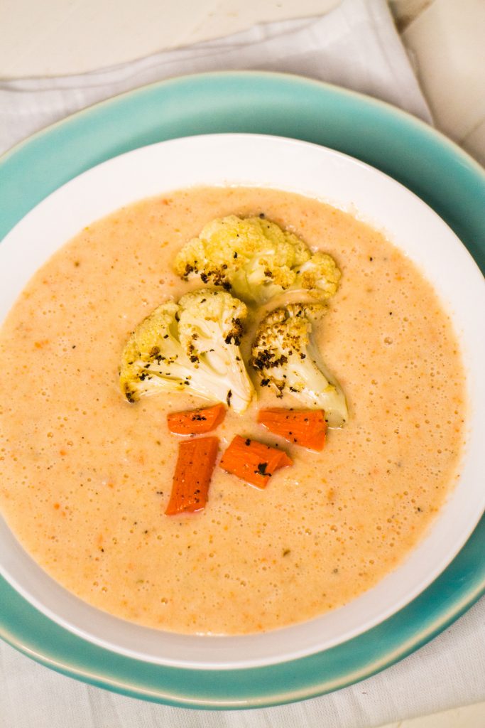 roasted cauliflower soup in white bowl with cauliflower and carrots on top.