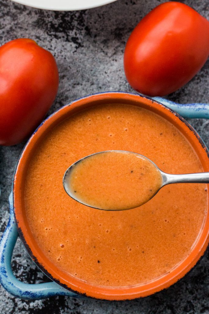 spoon filled with tomato soup in blue bowl. 