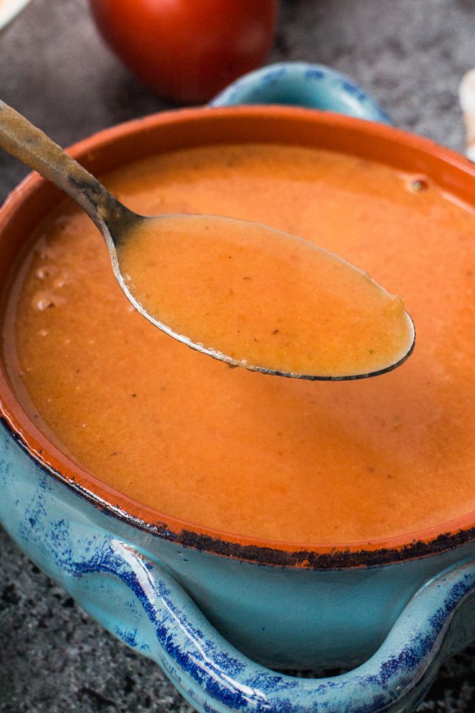 spoon going into blue bowl of fresh tomato soup.