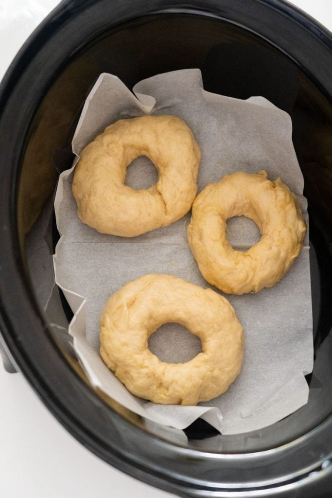 uncooked bagels in slow cooker on parchment paper