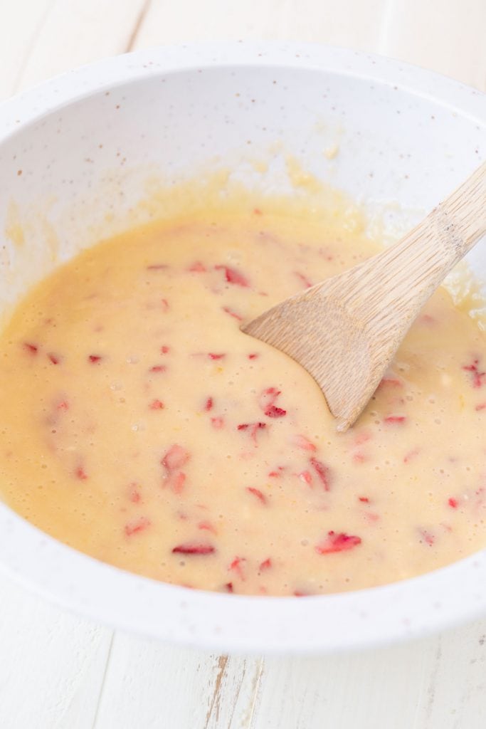 strawberries mixed into batter with wooden spoon