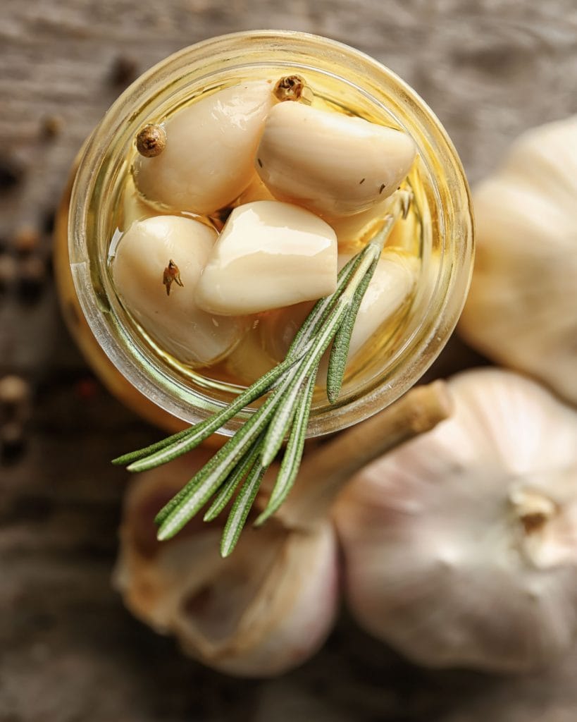 peeled garlic bulbs in olive oil with sprig of rosemary