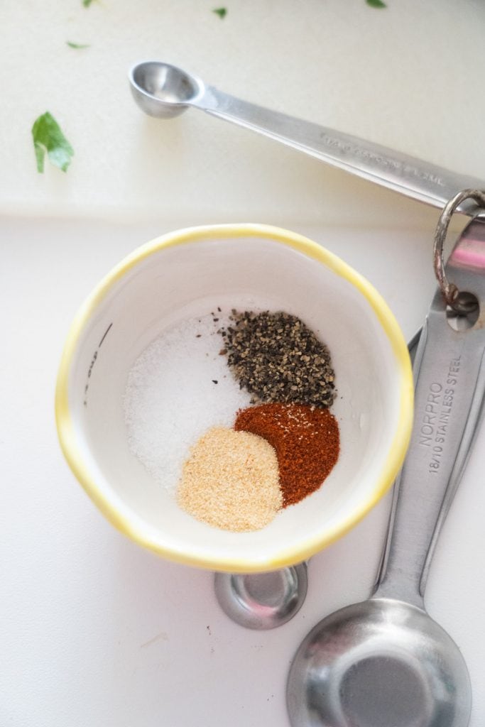 seasonings in small white bowl with measuring spoons next to it