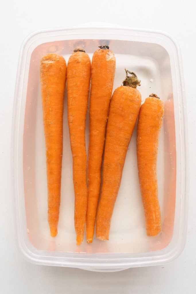 carrots being stored in water container with greens chopped off