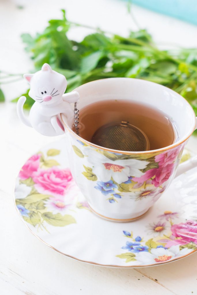 floral tea cup filled with parsley tea, cat themed infuser ball on side