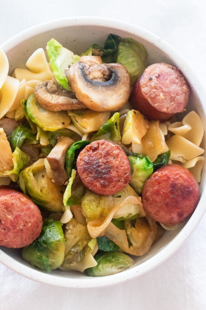 kielbasa, brussels sprouts and mushrooms over egg noodles in white bowl