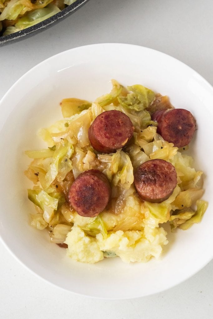 bowl of mashed potatoes with fried cabbage and sausage on top of it