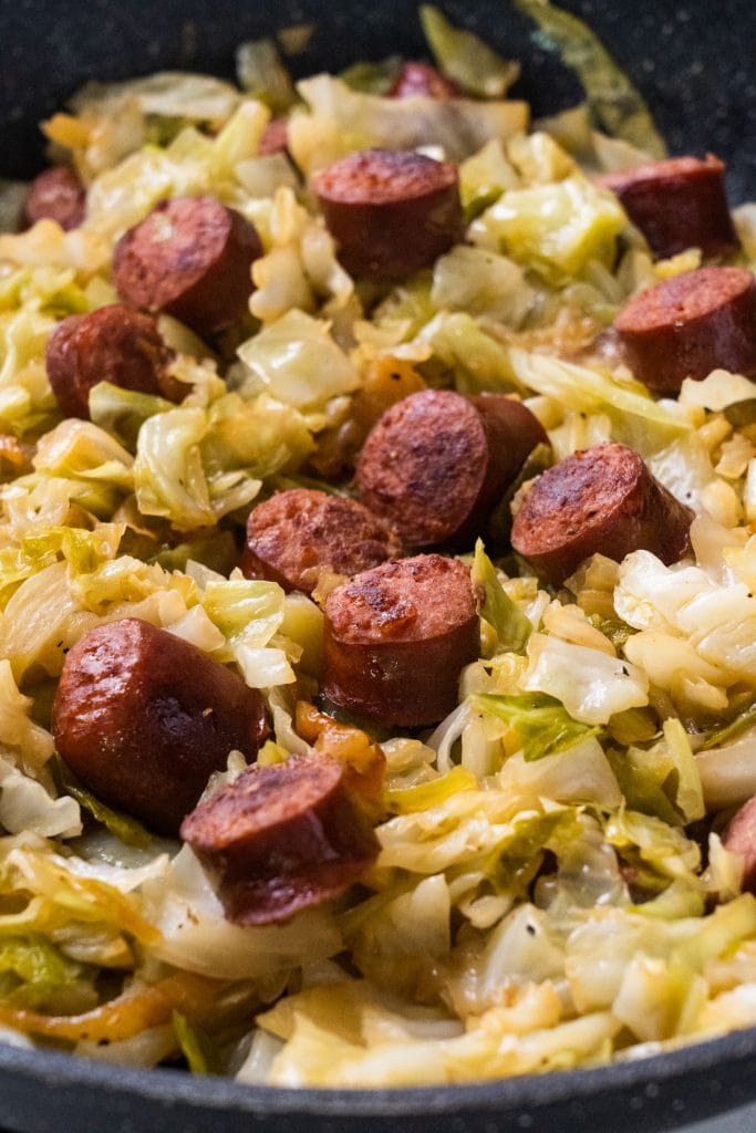 chopped up sausage with cabbage and onions in black skillet