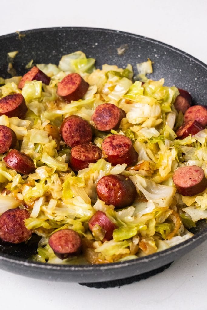 fried cabbage and sausage in black skillet on white background