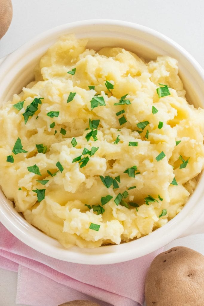 creamy mashed potatoes in white bowl with fresh parsley on top