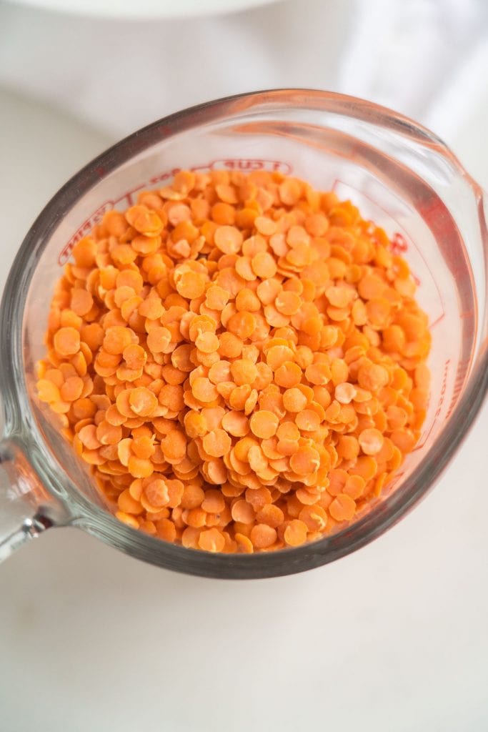 red lentils in glass  measuring cup on white background