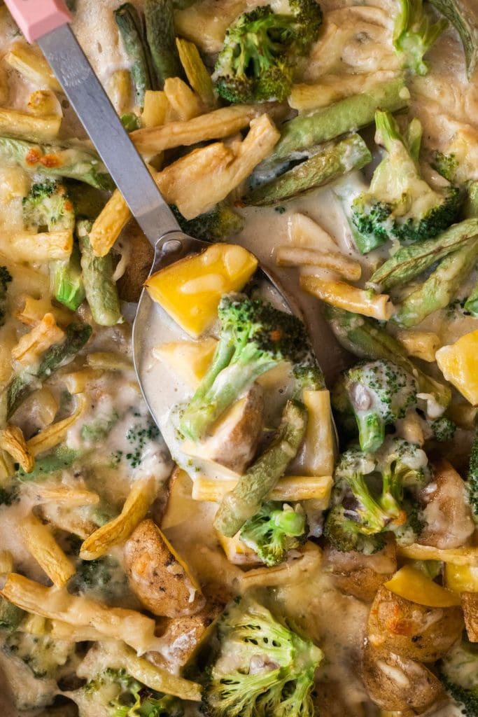spoon with broccoli, green beans and potatoes on it in baking dish with creamy casserole