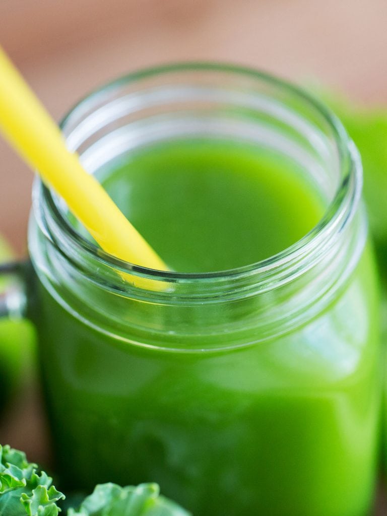 closeup of green juice in glass with yellow straw
