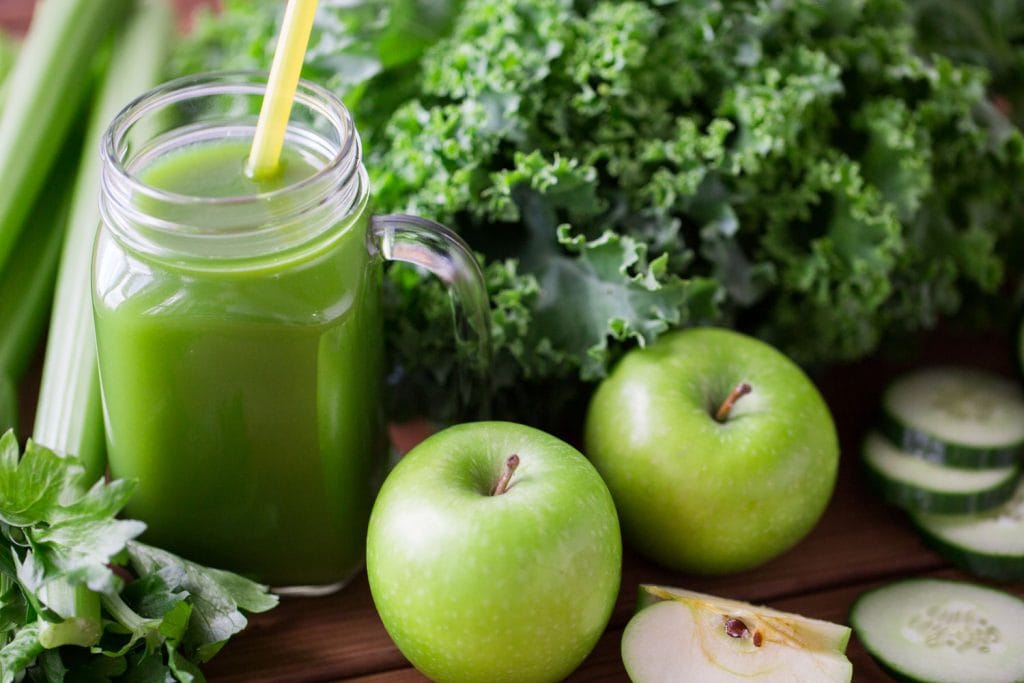 mason jar filled with green juice on table with celery, kale, cucumbers and green apples