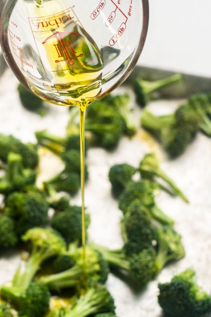 olive oil being poured over broccoli