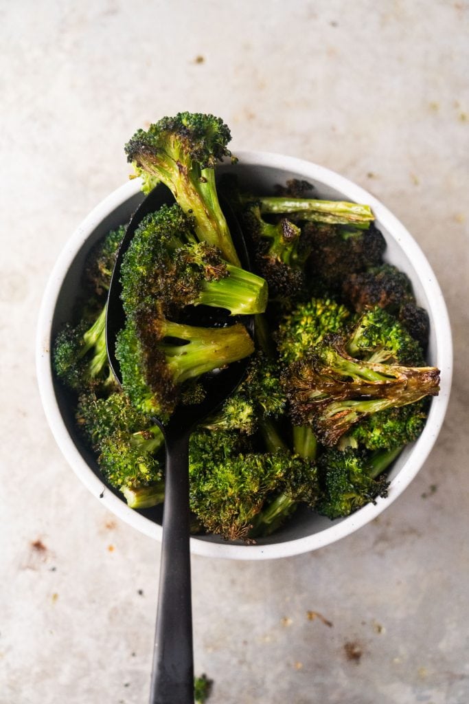white bowl filled with roasted broccoli with black spoon 