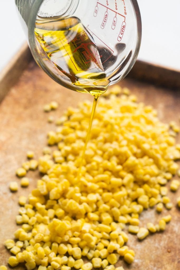 olive oil being poured on corn on baking sheet