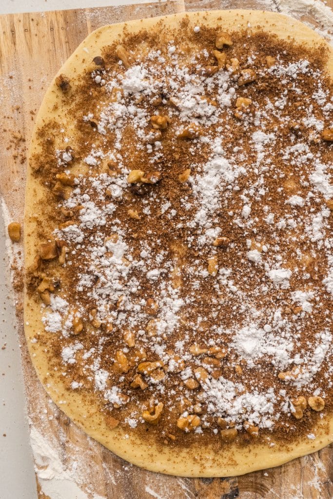 cinnamon sugar mixture with walnuts on top of bread dough on cutting board