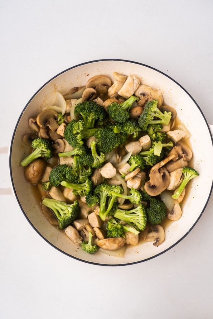 broccoli, broth, mushrooms, onion and chicken in white pan