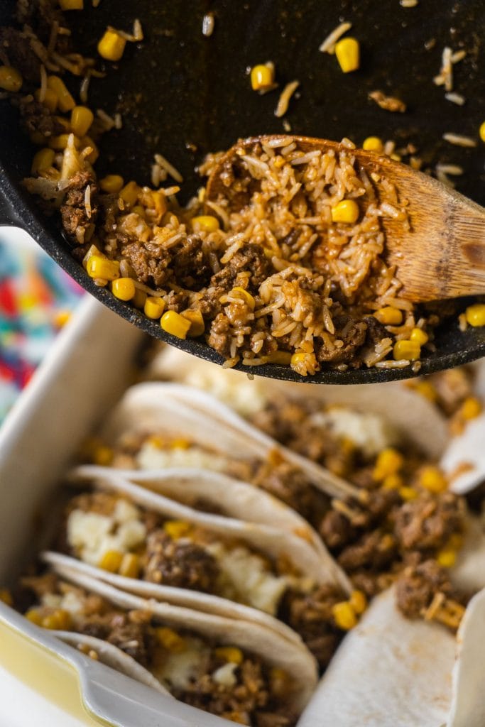 ground beef being poured from skillet on top of tacos.