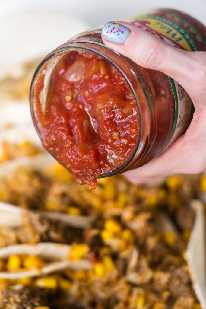jar or salsa being poured on top of tacos