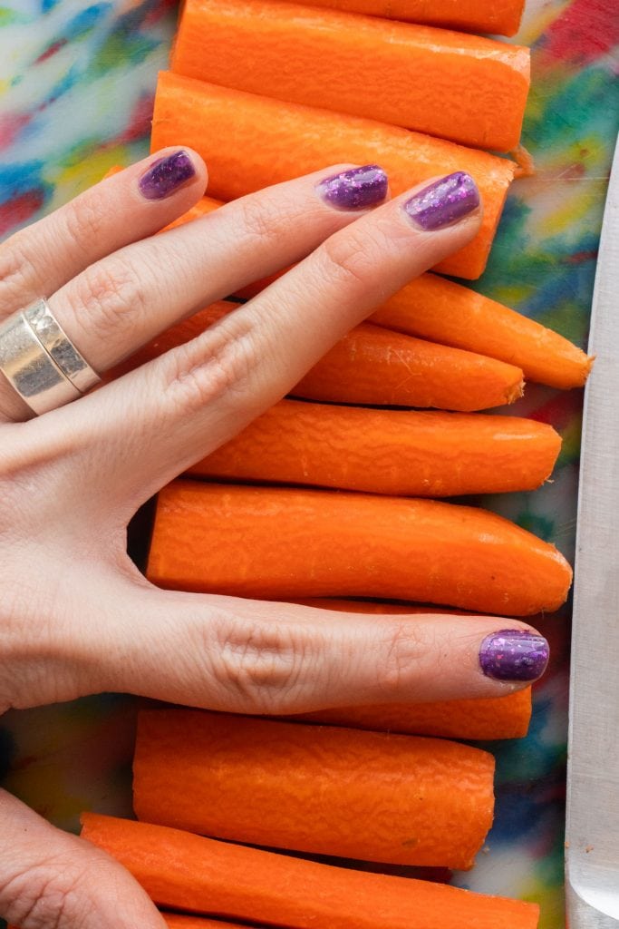 finger with purple nail polish next to carrots showing size.
