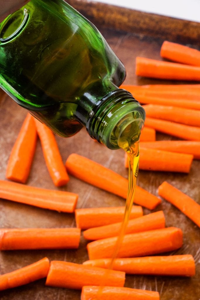 olive oil being poured on top of carrots.