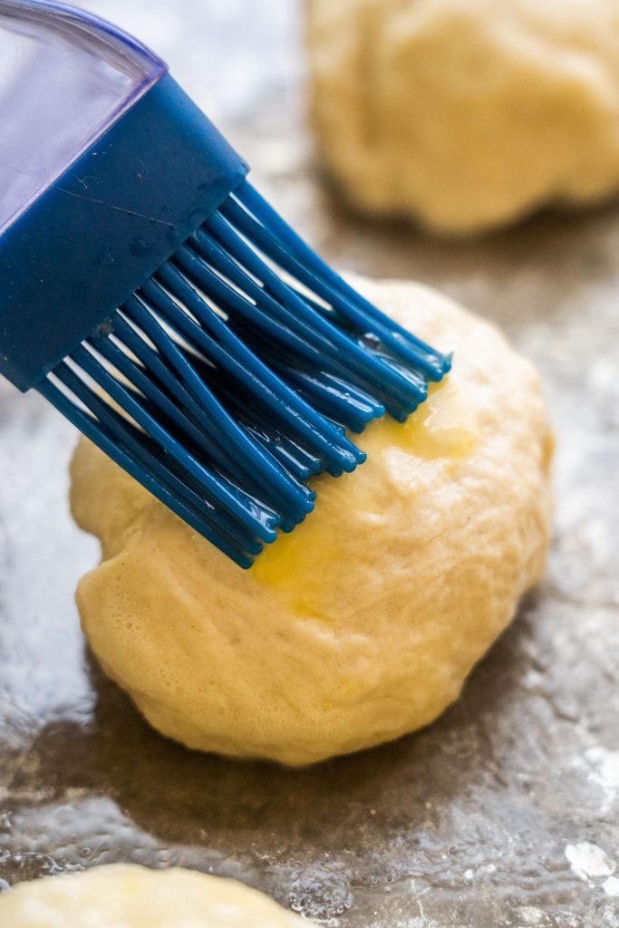 brush brushing butter on top of roll on baking sheet.