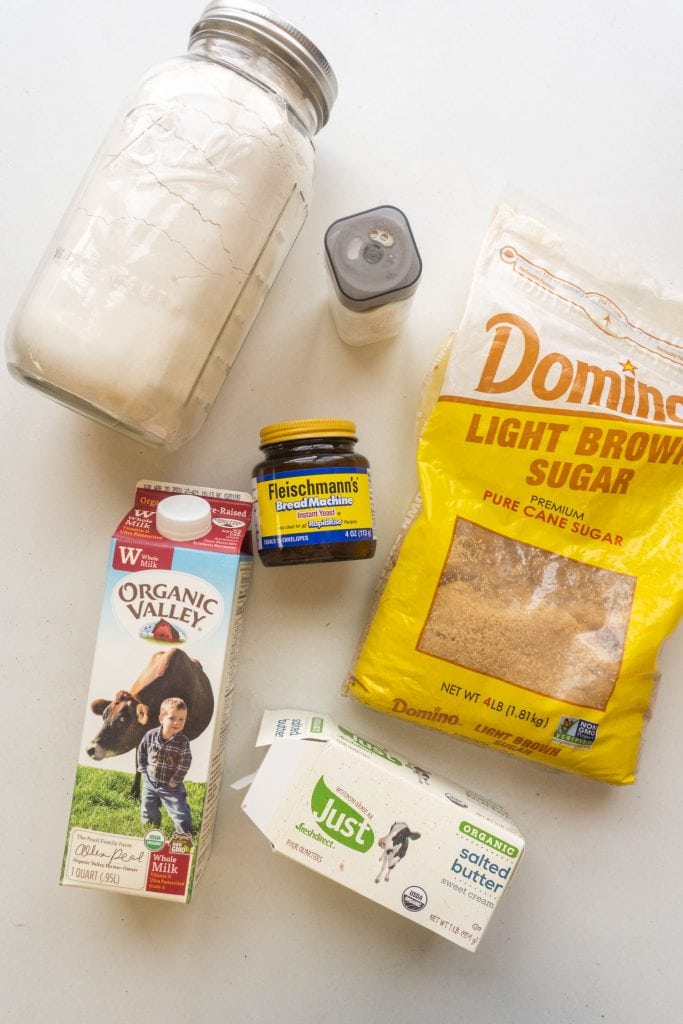 flour, salt, yeast, brown sugar, milk and butter on white table.