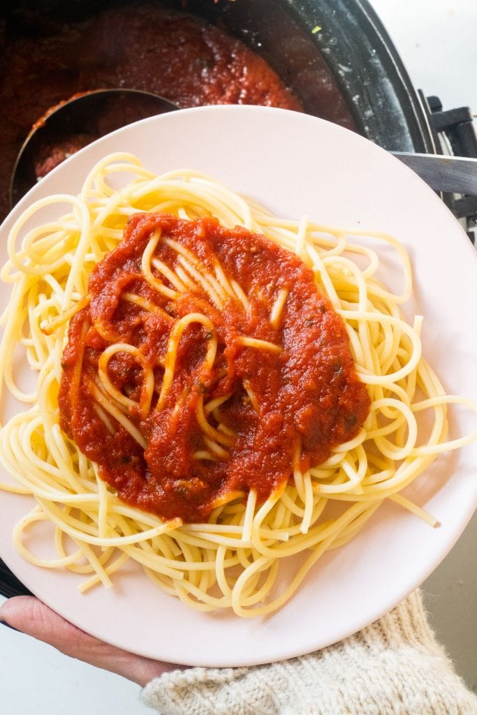 hand holding plate with spaghetti with spaghetti sauce on it.