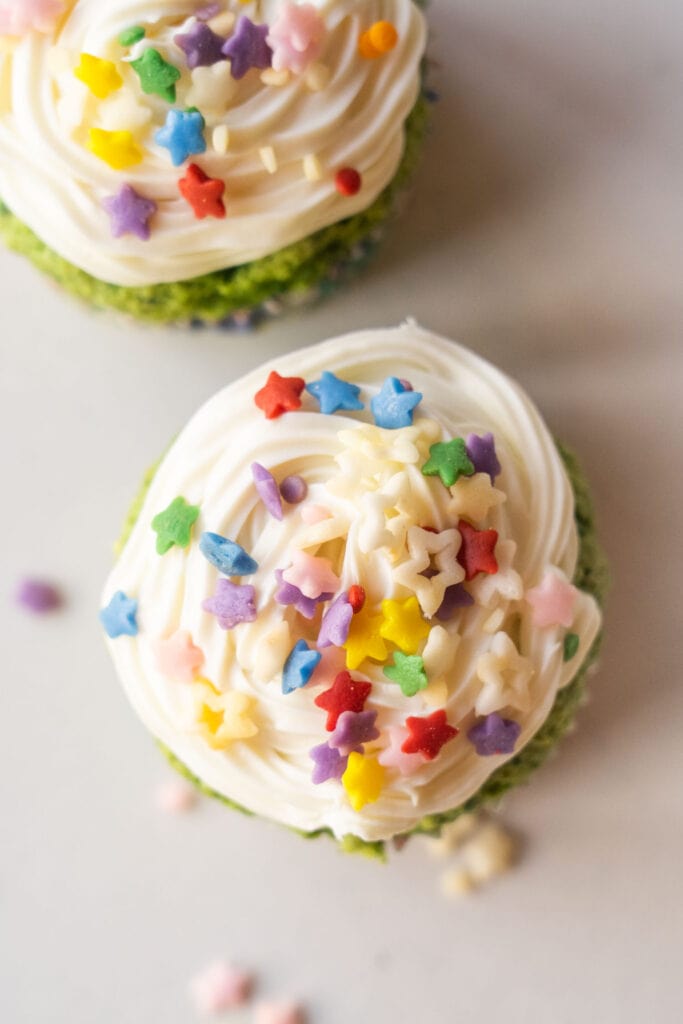 cupcake with white frosting and rainbow sprinkles on top.
