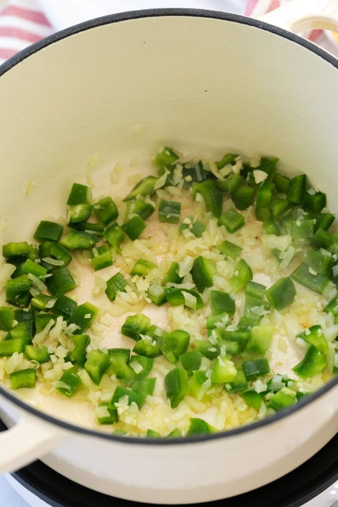 garlic, green pepper and onion in white pot being sauteed. 