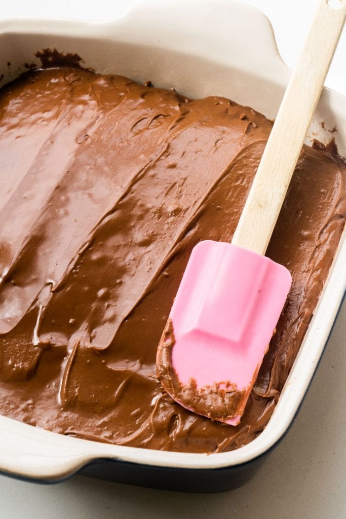 spatula spreading frosting on warm brownies.