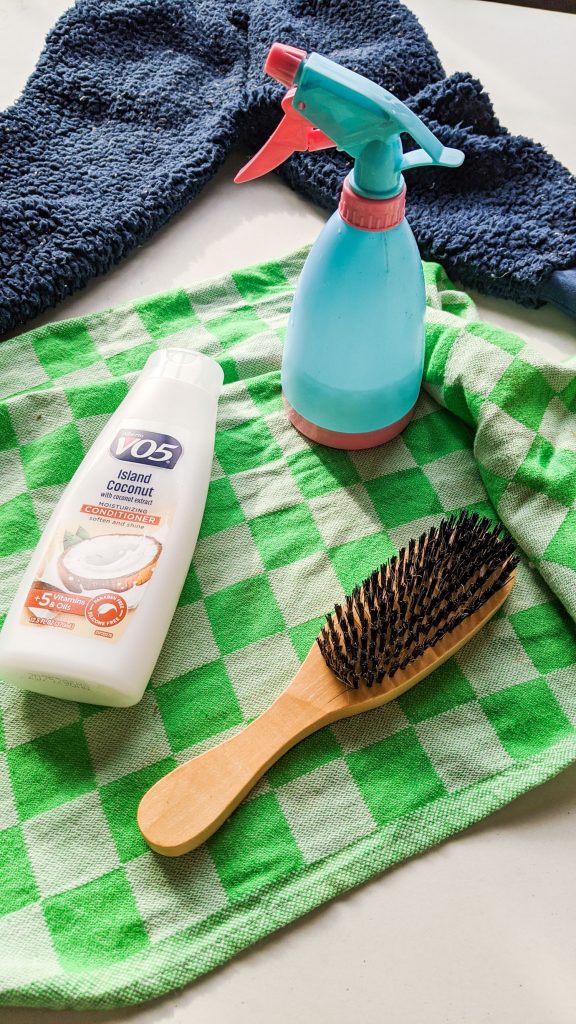 spray bottle, conditioner and brush on green towel on table.