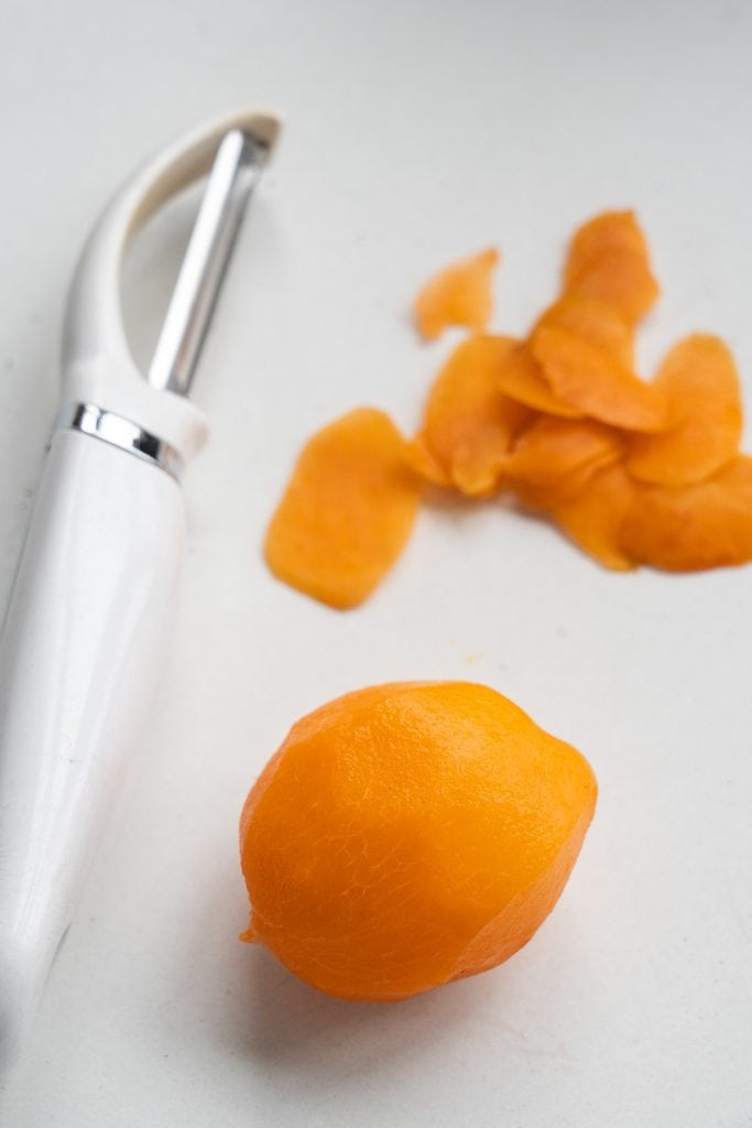 apricot peeled on table with vegetable peeler next to it.