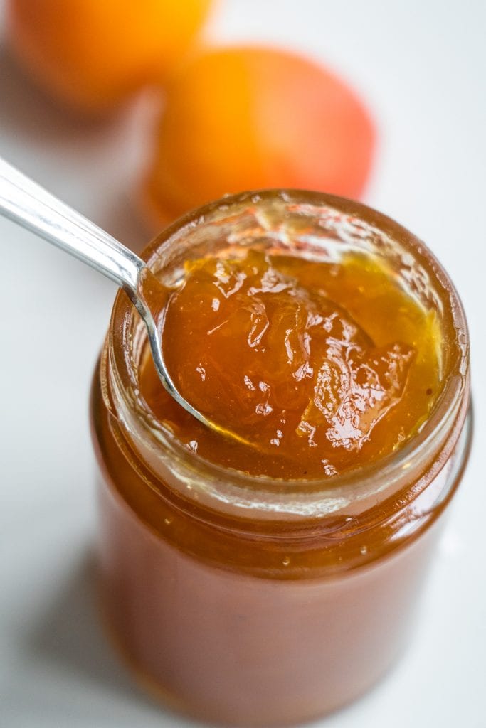 glass jar filled with apricot jam with spoon coming out of it.