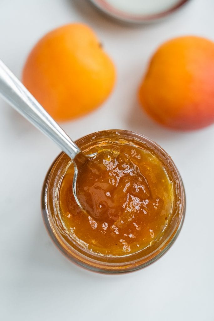 jar of apricot jam with spoon coming out of it.