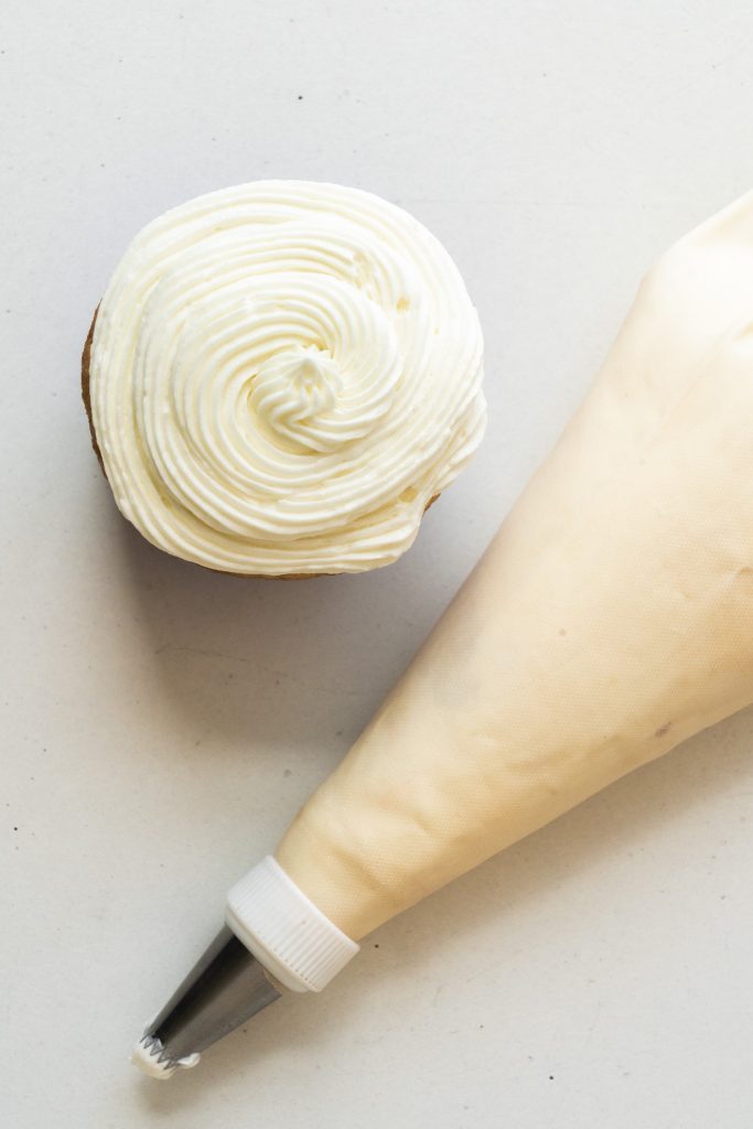 piping bag filled with frosting with cupcake next to it.