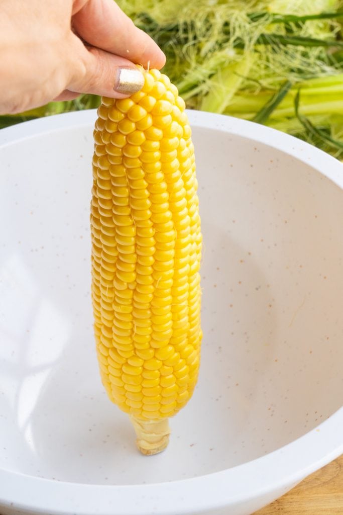 hand holding up cob of corn in bowl. 