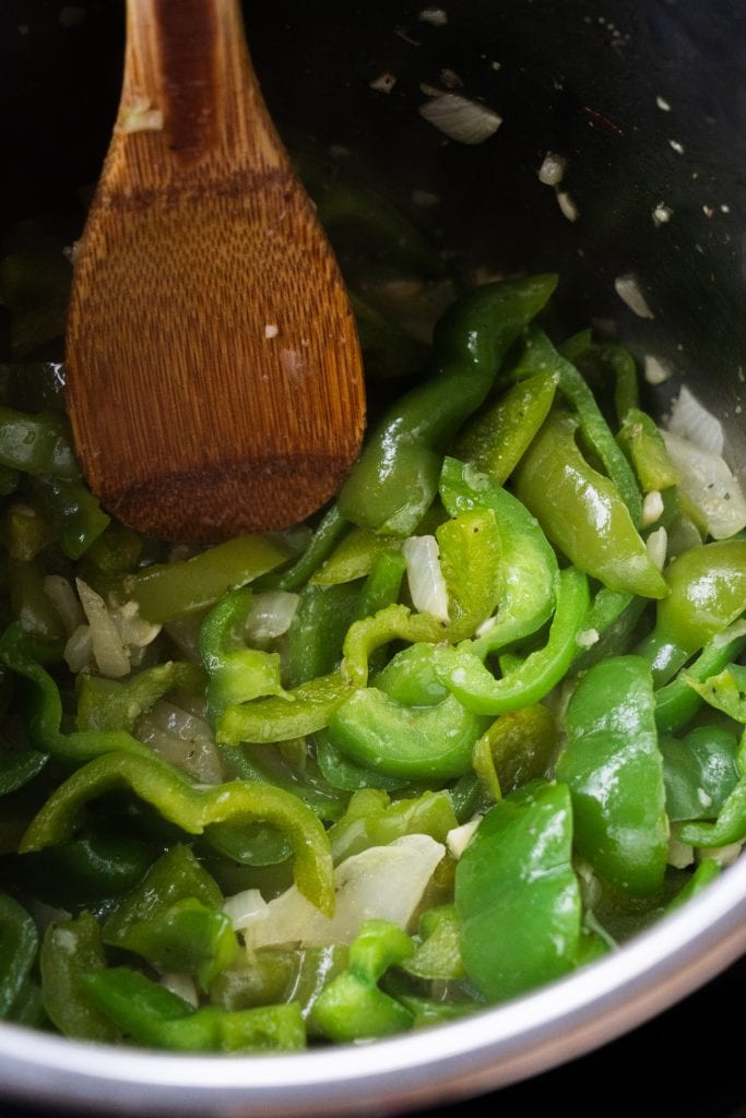 green peppers, onion and garlic in instant pot with spoon stirring them.