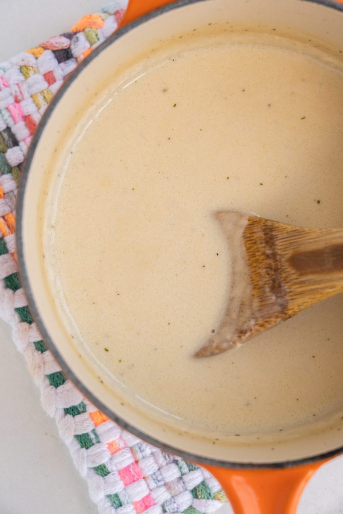 spoon stirring creamy sauce in orange saucepan.