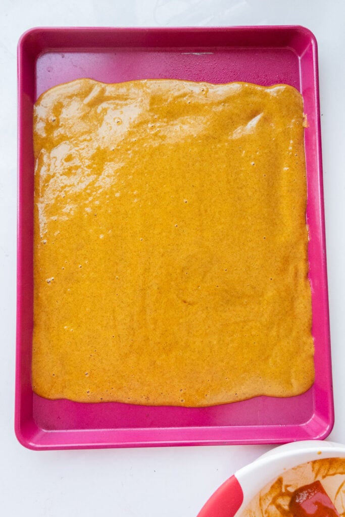 pumpkin cake batter spread out on baking sheet.