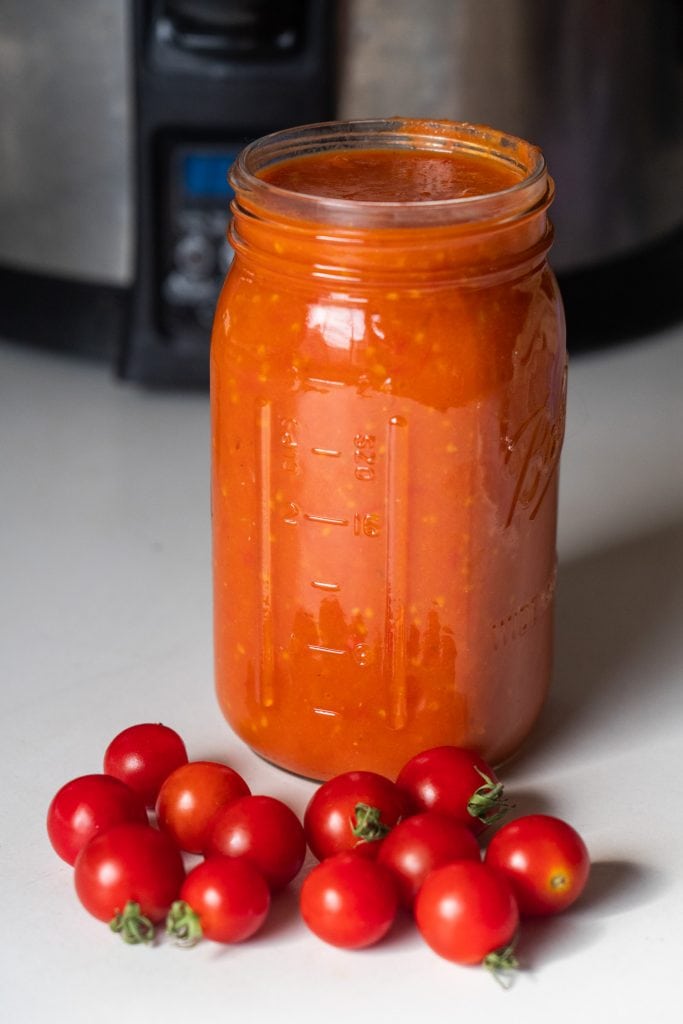 jar of cherry tomato sauce sitting in front of slow cooker on table.