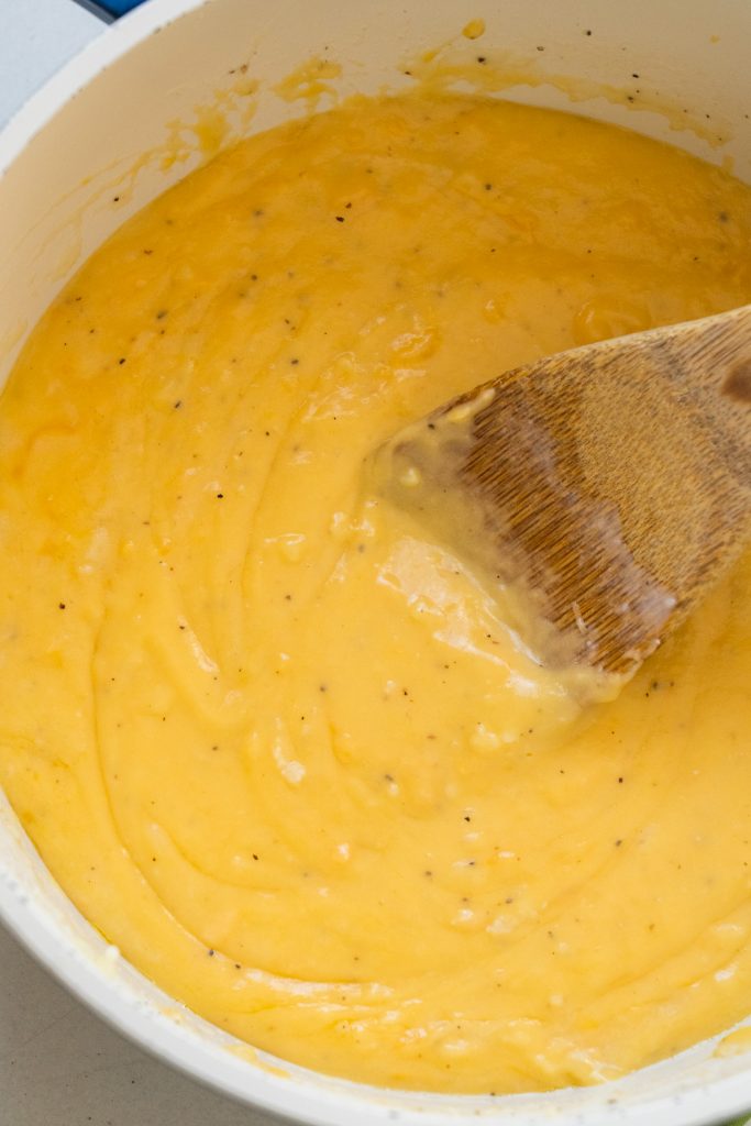 cheese sauce in saucepan with spoon stirring it.