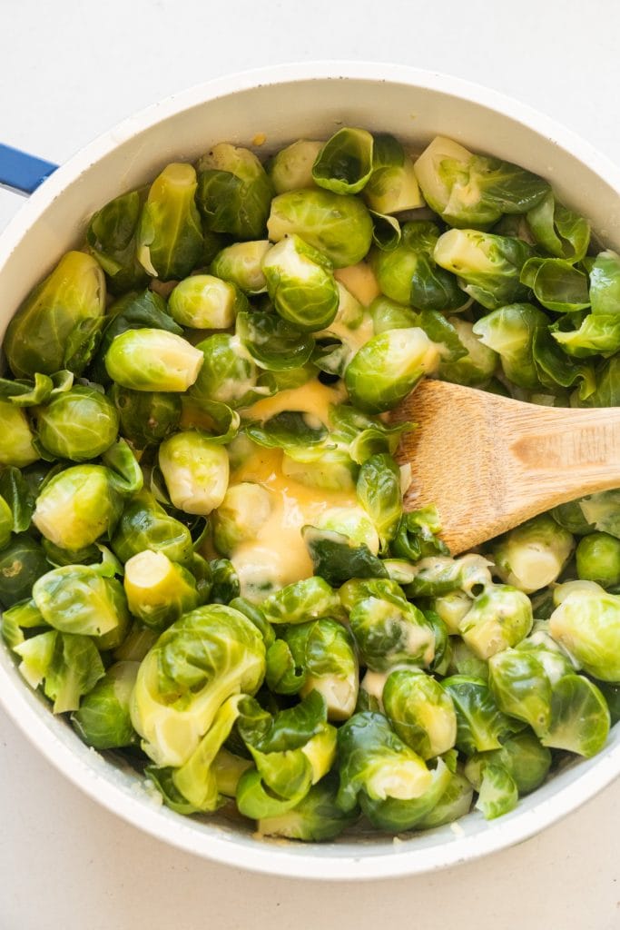 spoon mixing brussels sprouts in cheese sauce in saucepan.