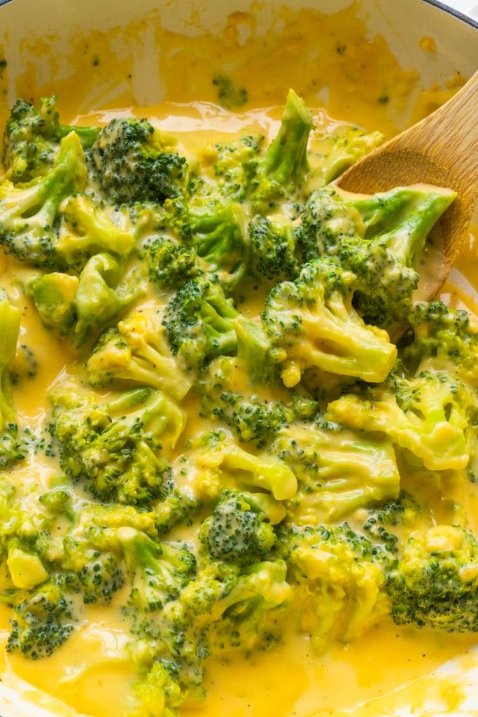 spoon stirring broccoli with cheese sauce.