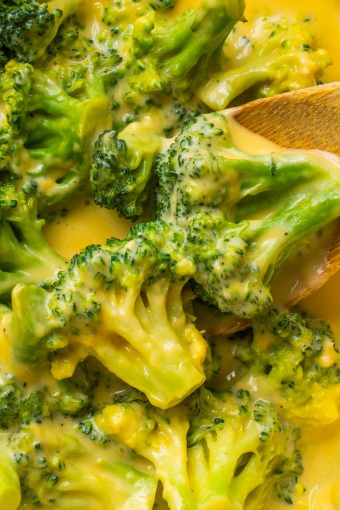 wooden spoon filled with broccoli with cheese in pan.