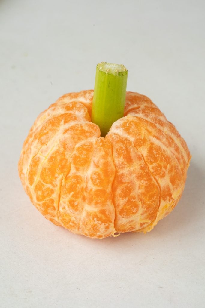 orange with celery stick in the middle, looking like a pumpkin.