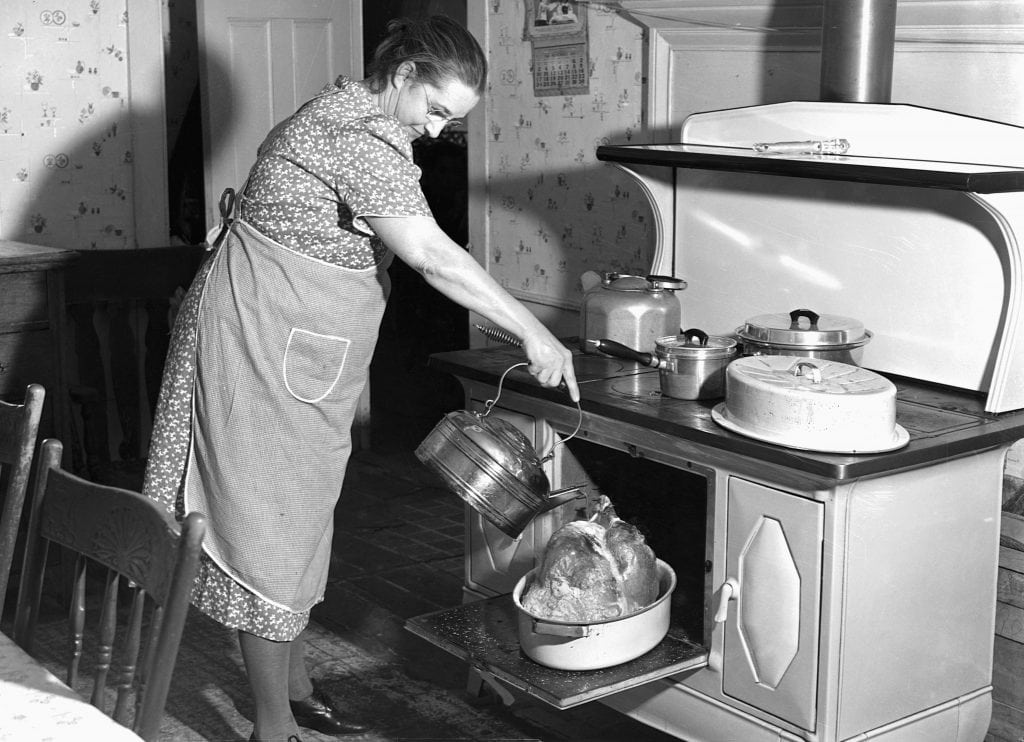 vintage photo of older woman basting turkey in oven. 
